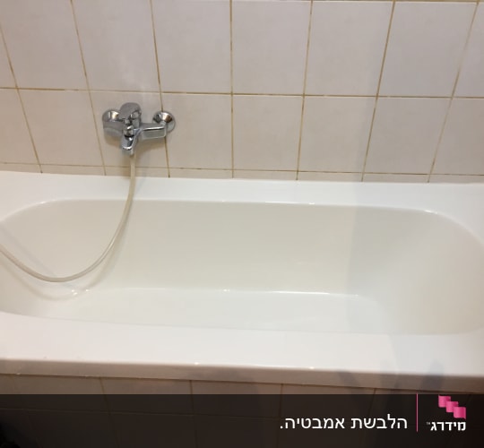 אמבטיה לבנה עם ברז וכיסוי קרמיקה על הקיר